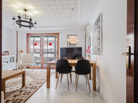 Open living-dining room with a wooden table and six black chairs, a chandelier, and large glass doors to a balcony.