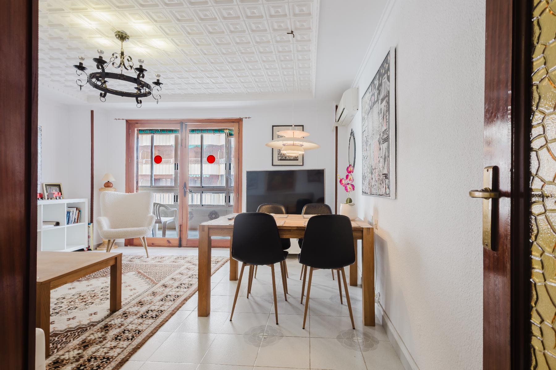 Open living-dining room with a wooden table and six black chairs, a chandelier, and large glass doors to a balcony.