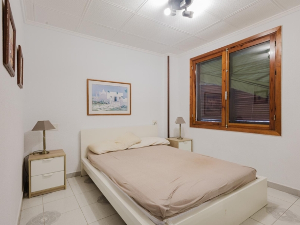 Bedroom with a low white bed, beige bedding, and two matching nightstands with lamps on either side.