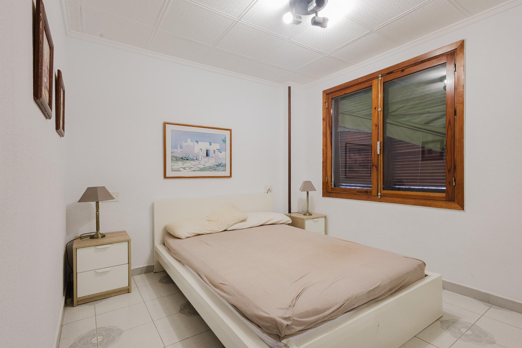 Bedroom with a low white bed, beige bedding, and two matching nightstands with lamps on either side.