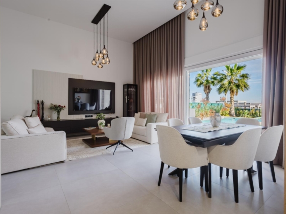 Bright modern living room with white sofas, TV wall, and a glass door to a pool area with palm trees.