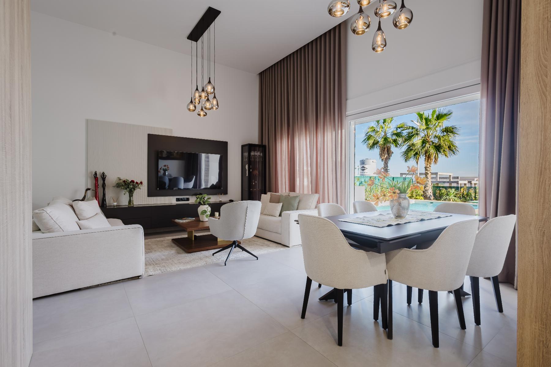 Bright modern living room with white sofas, TV wall, and a glass door to a pool area with palm trees.
