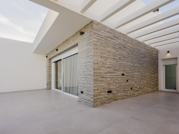 Modern outdoor patio with a stone veneer wall, sliding glass doors, and a white slatted pergola.
