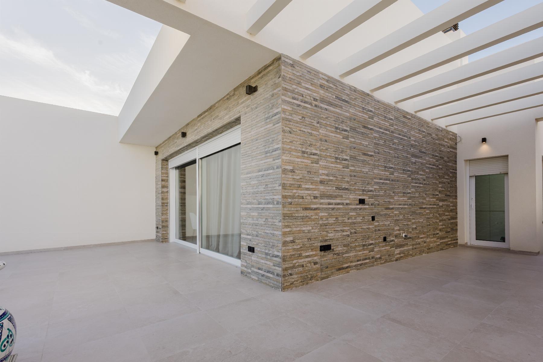 Modern outdoor patio with a stone veneer wall, sliding glass doors, and a white slatted pergola.