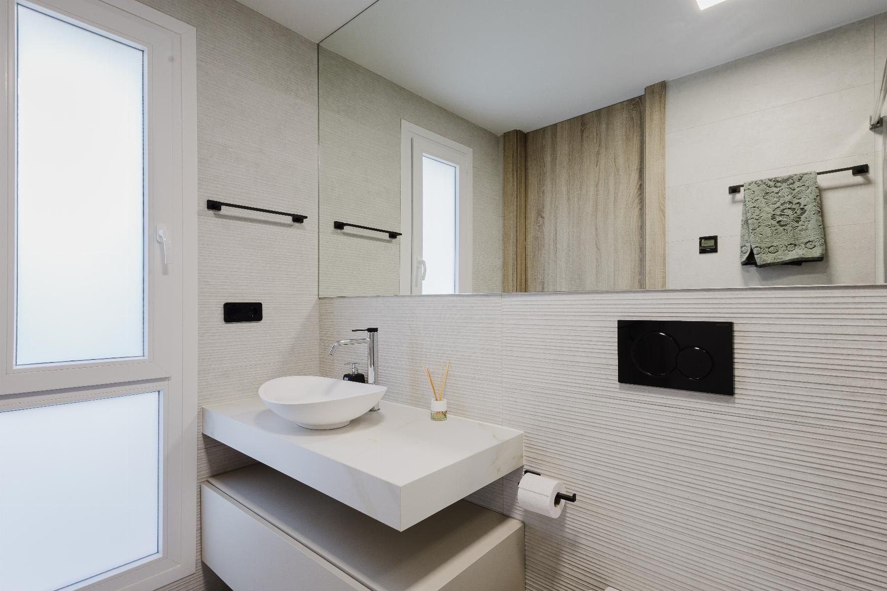 Contemporary bathroom with frosted windows, wall-mounted storage cabinets, and a large mirror reflecting a wooden panel accent.