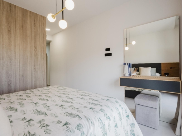 Bright bedroom with a large wood wardrobe, patterned duvet, and a wall mirror above a vanity desk on the right.