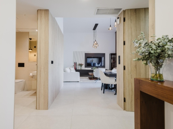 Open living area seen through wooden room dividers, with a white sofa, coffee table, TV, and hanging pendant lights in a modern home interior on a bright day