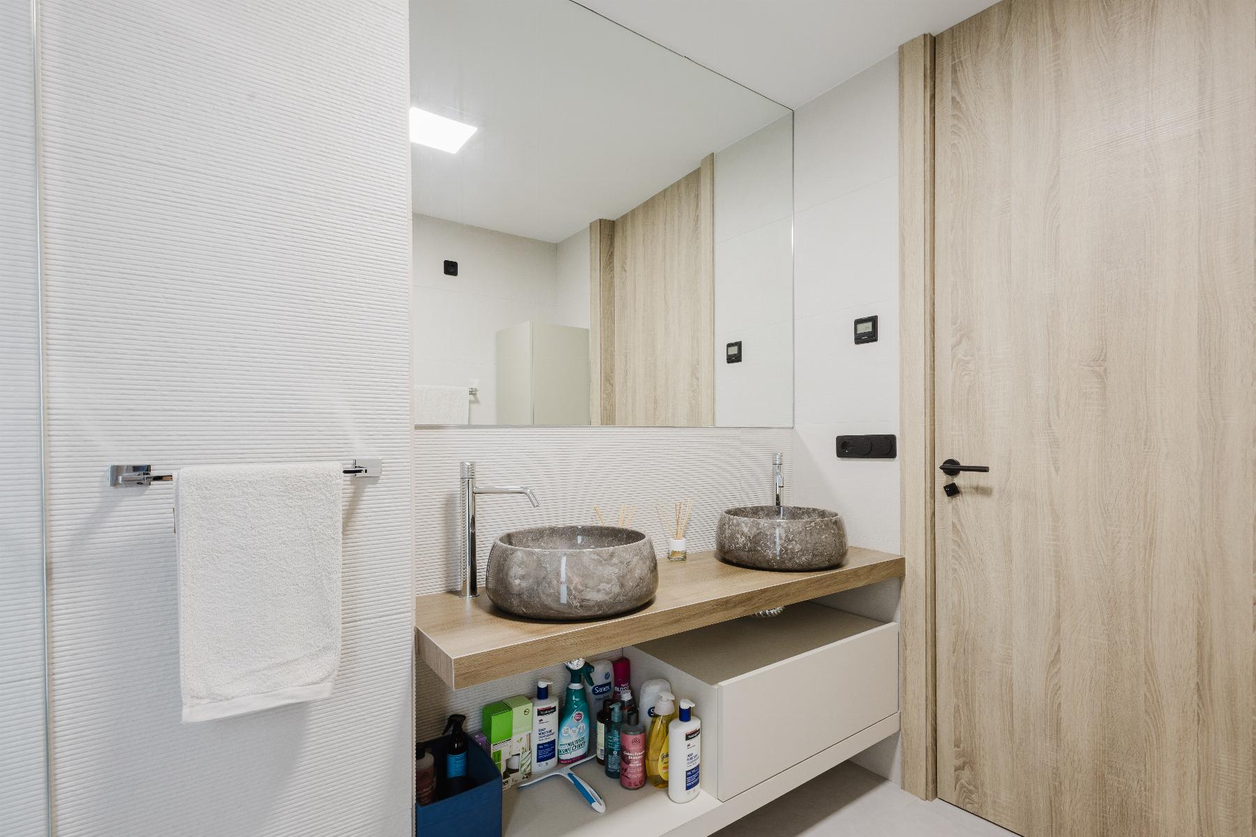Modern bathroom with two round stone vessel sinks on a wooden countertop and a large mirror above the sinks.