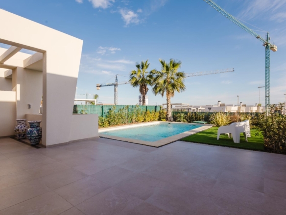 Modern poolside courtyard with palm trees, white walls, and construction cranes in the distance under a blue sky.