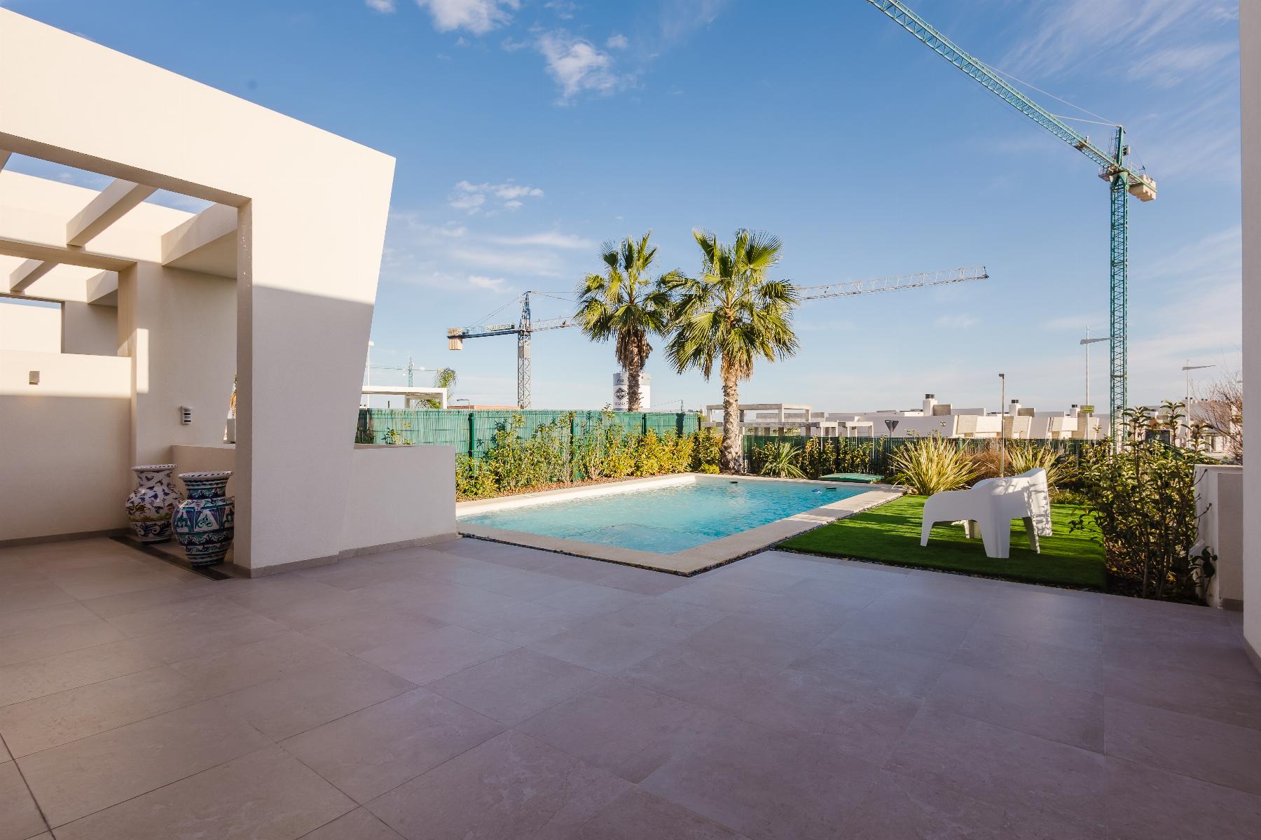 Modern poolside courtyard with palm trees, white walls, and construction cranes in the distance under a blue sky.