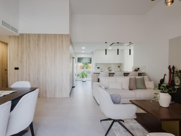 Open-concept living area with a light gray sofa and pastel cushions, facing a wood-accent partition and modern white kitchen in the background