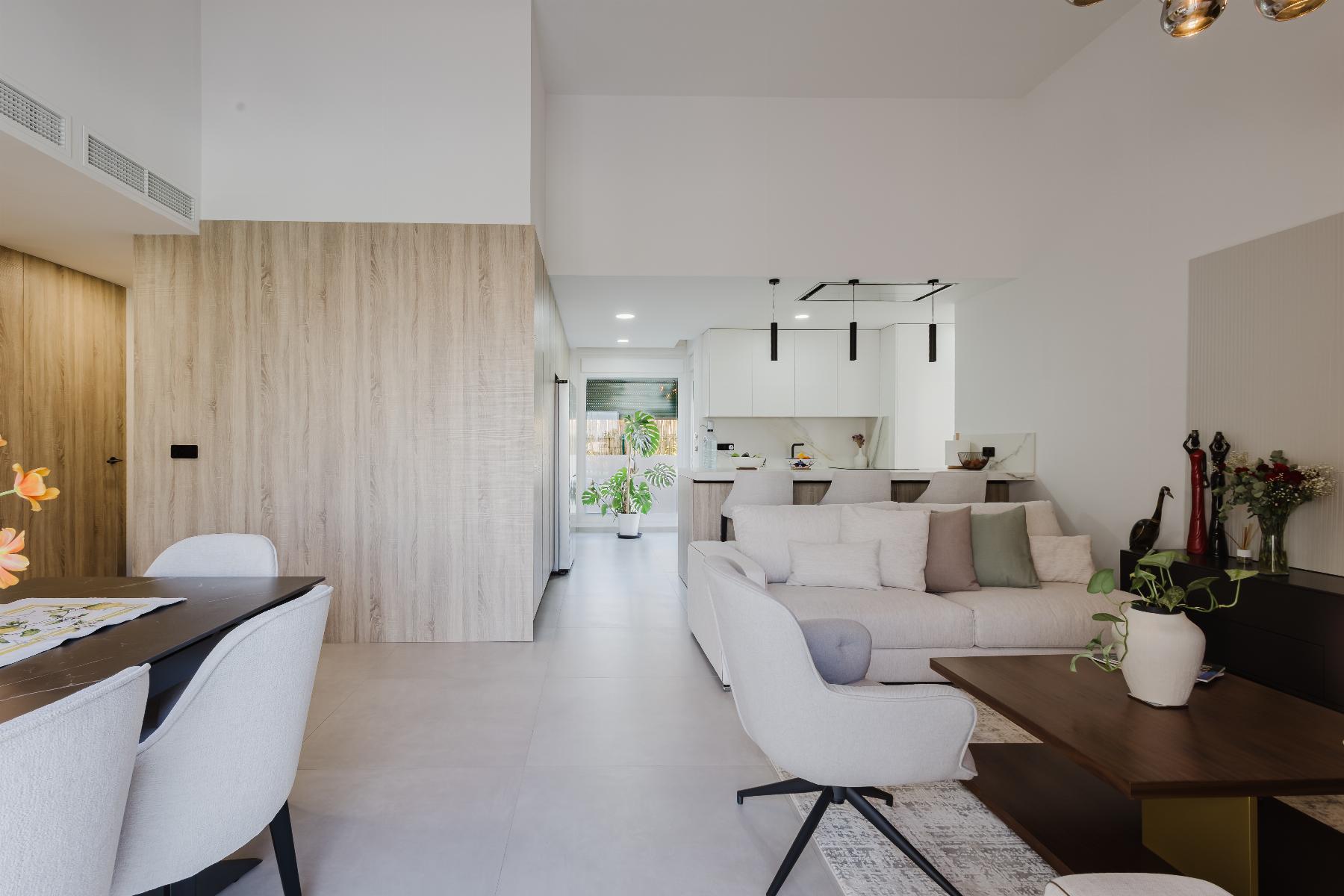 Open-concept living area with a light gray sofa and pastel cushions, facing a wood-accent partition and modern white kitchen in the background