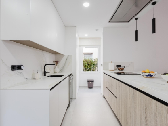 Bright minimalist kitchen with white cabinets, marble countertops, and a two-tone island; fruit bowls on the counter.