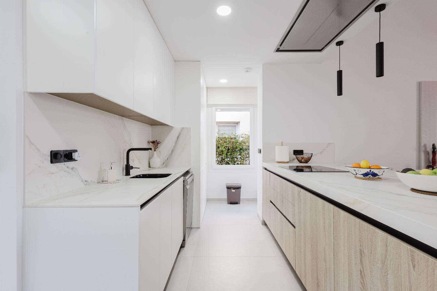 Bright minimalist kitchen with white cabinets, marble countertops, and a two-tone island; fruit bowls on the counter.