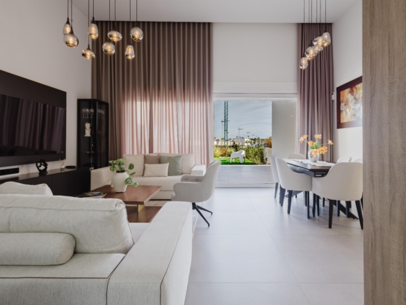 Open-concept living and dining room with cream sofas, pendant lights, and a large window showing a garden outside