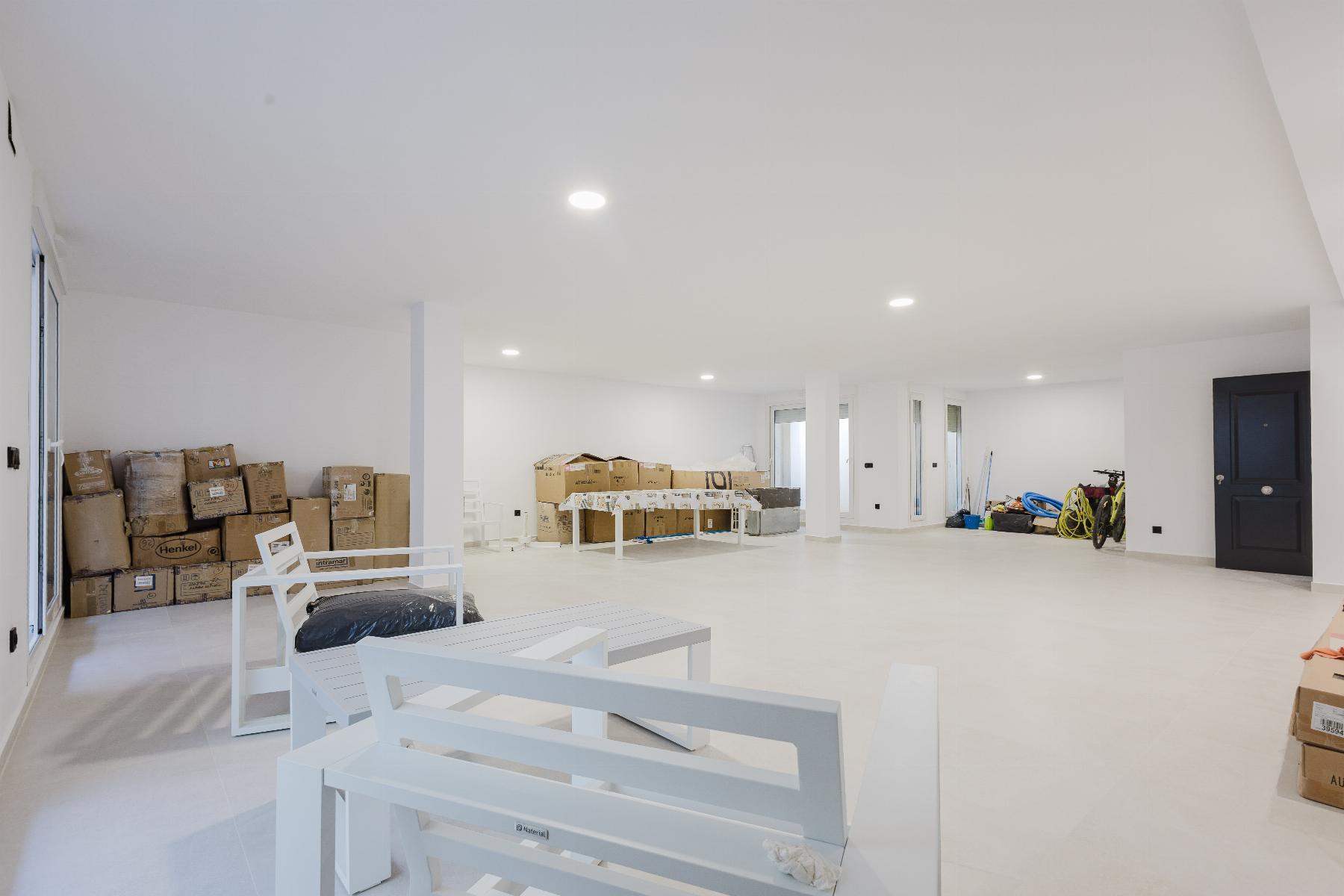Large, bright unfinished basement/garage with stacked cardboard boxes along left wall and white outdoor furniture in the foreground; dark blue door on the right.