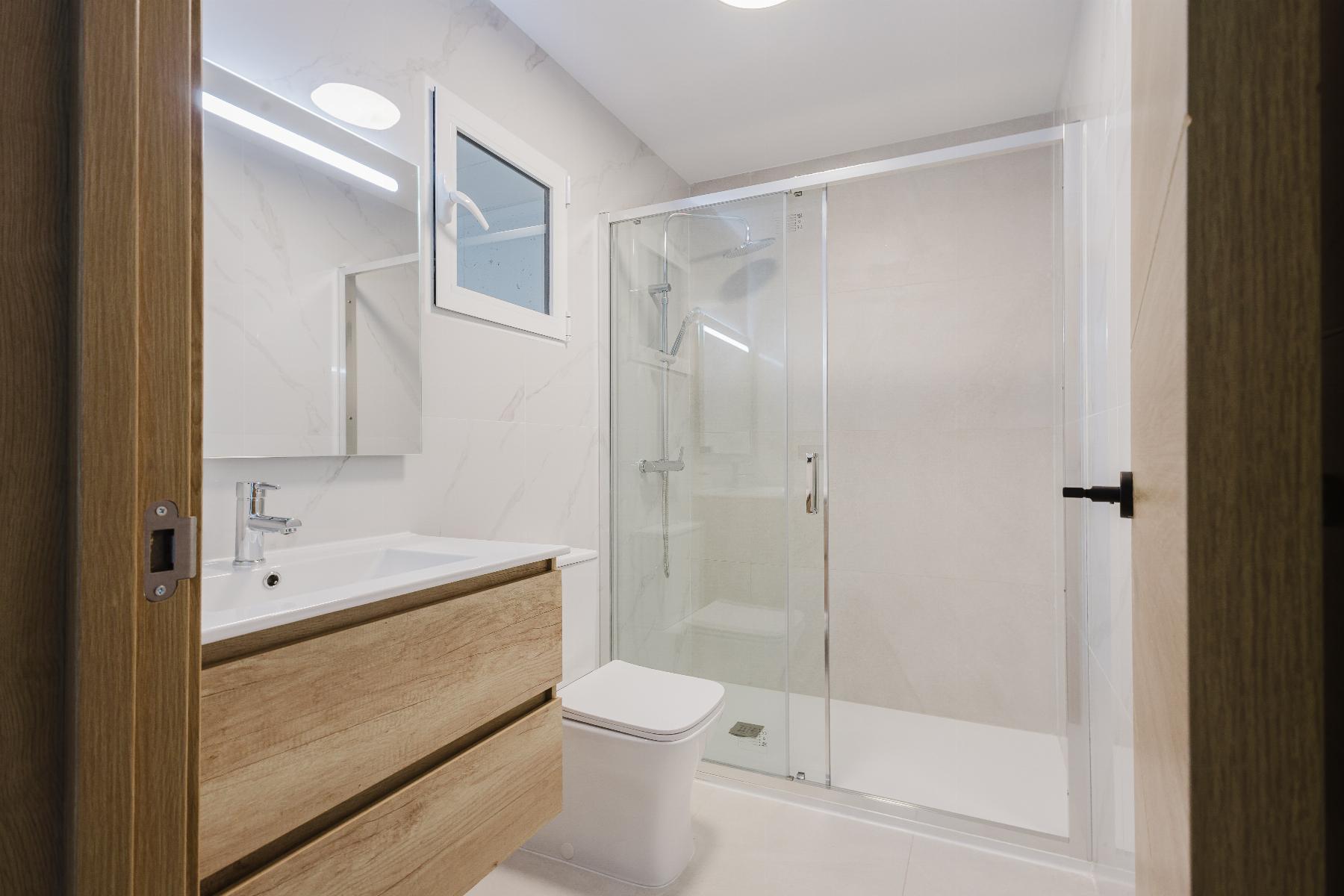 Modern bathroom with a glass shower enclosure, white fixtures, and a light wood vanity against marble walls.