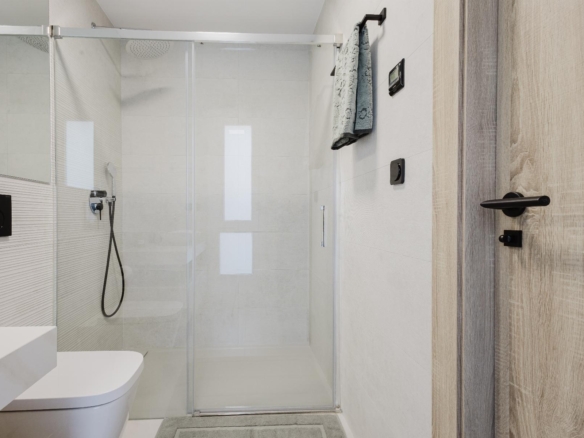Modern bathroom with a glass shower enclosure, wall-hung toilet, and light wood door on the right.