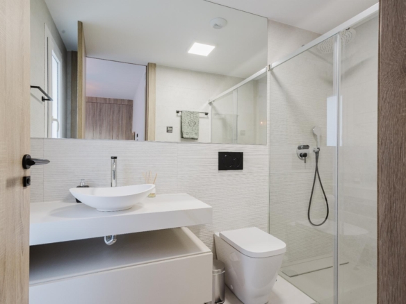 Modern bathroom with wall-mounted vanity, white vessel sink, and chrome faucet facing a large mirror and glass shower enclosure.