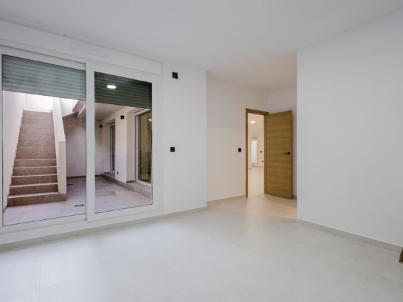 Empty white room with large glass sliding doors opening to a courtyard and exterior stairs visible outside in daylight.