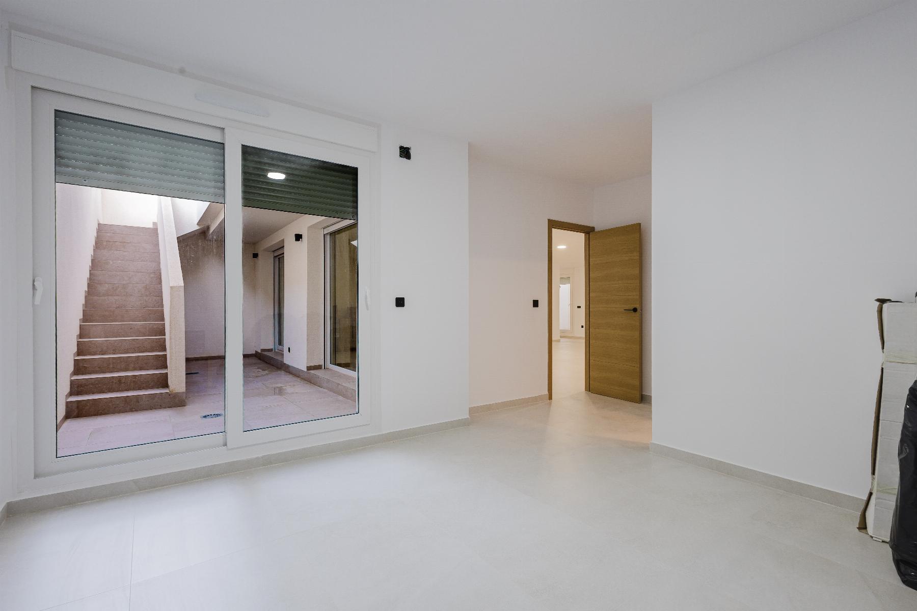 Empty white room with large glass sliding doors opening to a courtyard and exterior stairs visible outside in daylight.