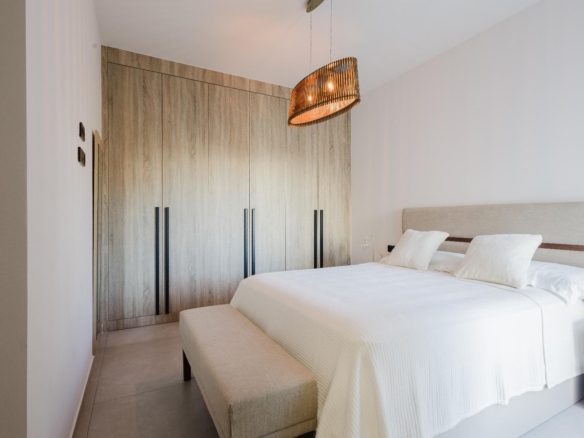 Modern bedroom with a tall wooden wardrobe wall, white bedding, and a woven drum pendant light above the bed
