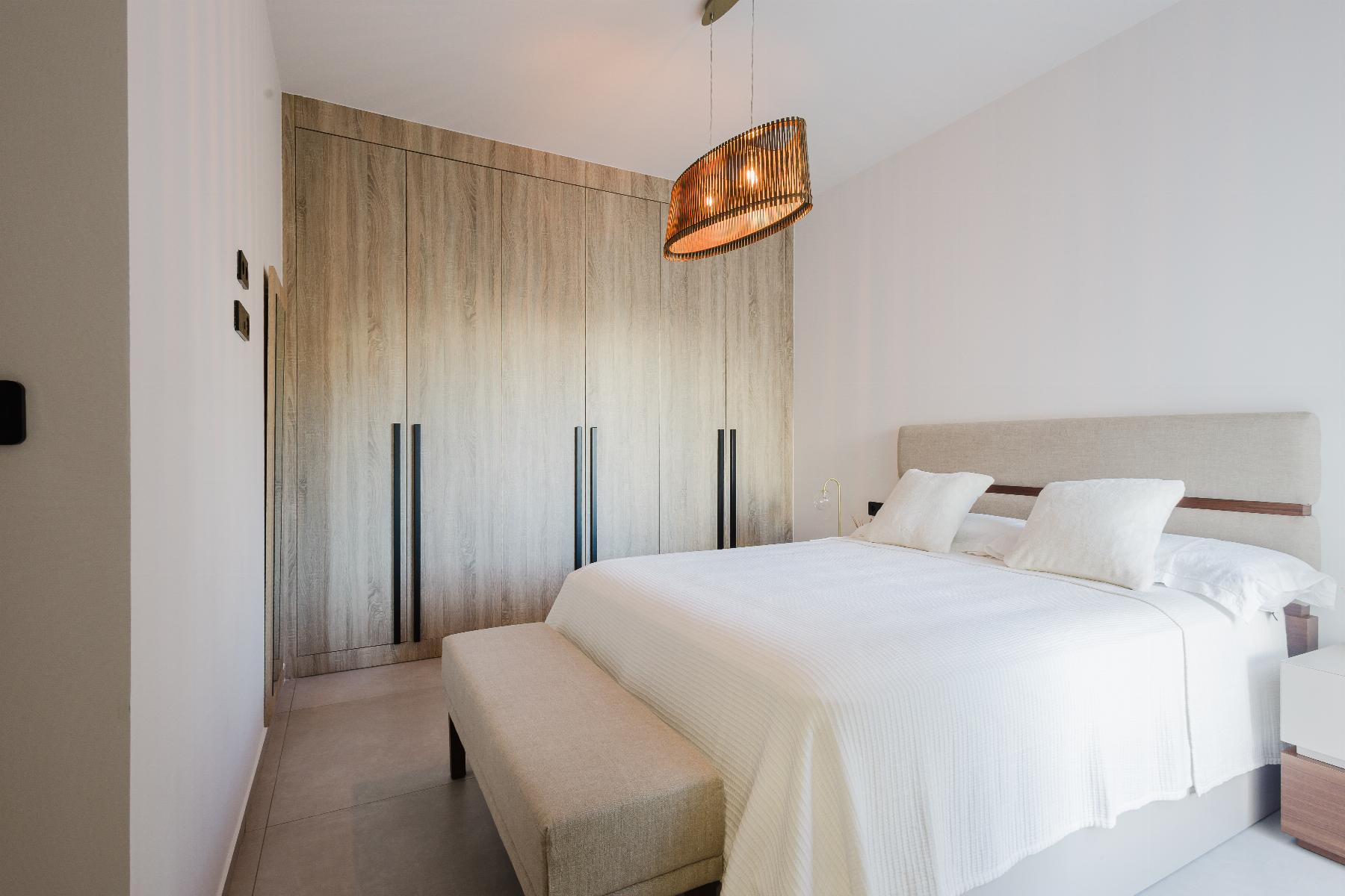 Modern bedroom with a tall wooden wardrobe wall, white bedding, and a woven drum pendant light above the bed