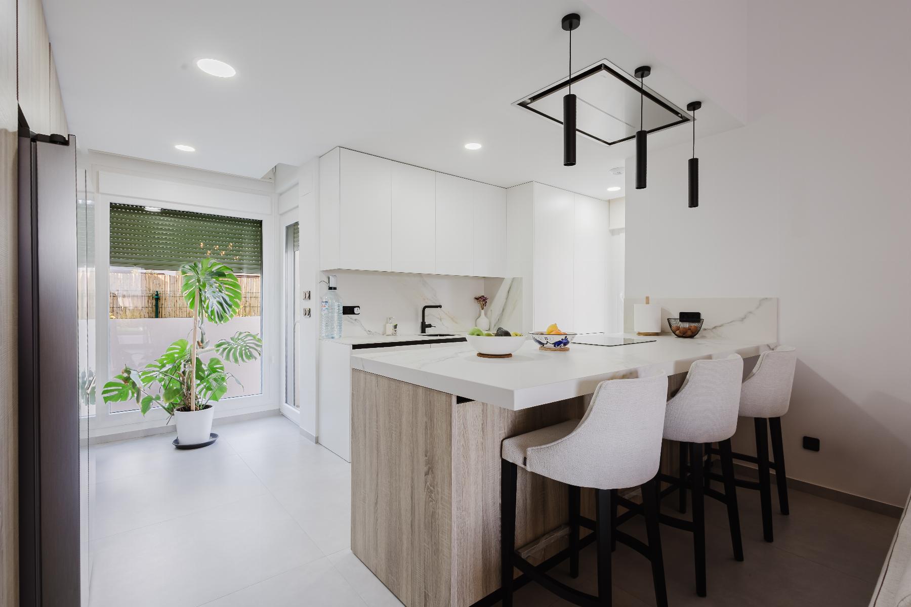 Bright modern kitchen with white cabinets, marble backsplash, and a wooden island island bar with beige stools.