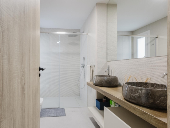 Contemporary bathroom with a wooden vanity, two stone vessel sinks, a large mirror, and a glass-enclosed shower.