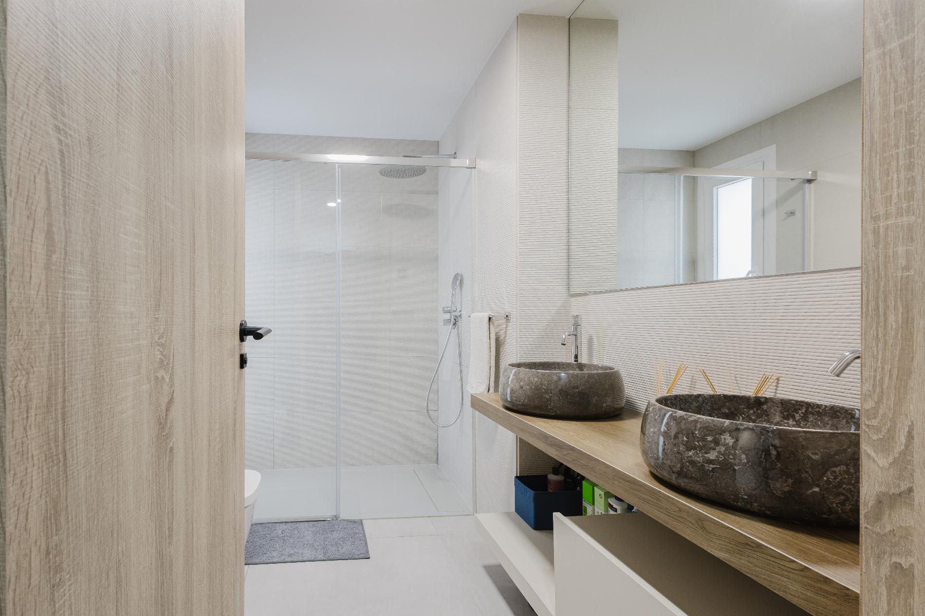 Contemporary bathroom with a wooden vanity, two stone vessel sinks, a large mirror, and a glass-enclosed shower.