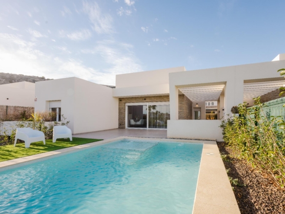 Modern white villa with a rectangular pool, glass doors, and a shaded patio area under a blue sky.
