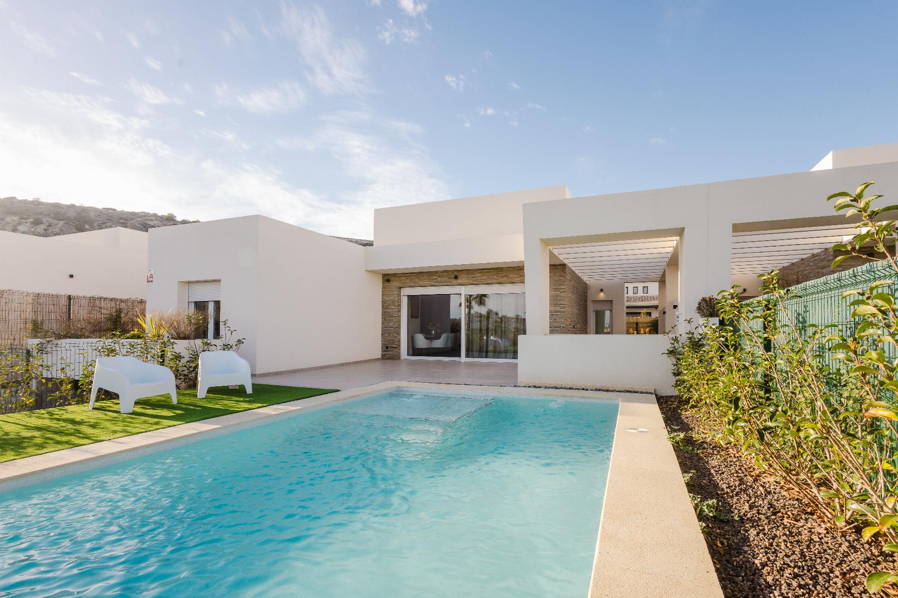 Modern white villa with a rectangular pool, glass doors, and a shaded patio area under a blue sky.