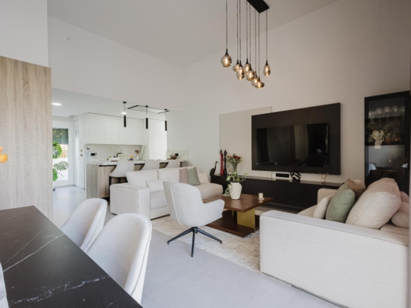 Open-concept living area with beige sofas, a large flat-screen TV on a dark wall panel, and a cluster of hanging pendant lights.