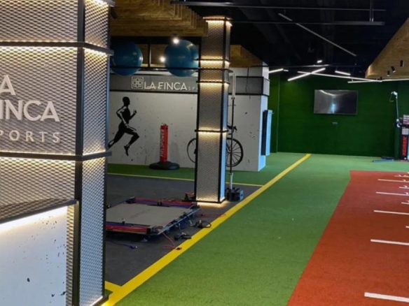Indoor sports facility corridor with a red running track and numbered lanes, green turf, and La Finca Sports branding on the left wall