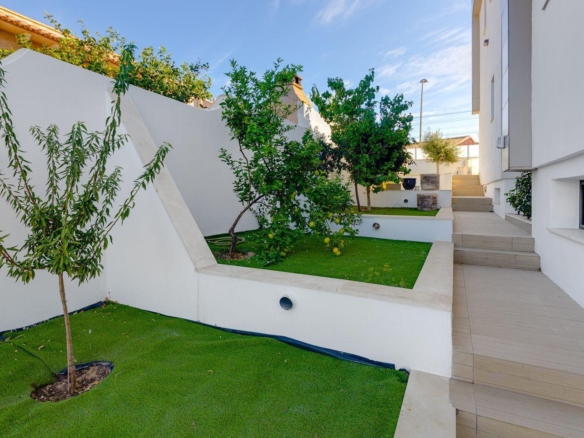 Modern courtyard with white walls, beige tiled steps, and raised planters containing small trees along a white building.