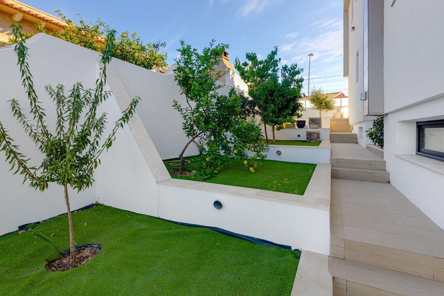 Modern courtyard with white walls, beige tiled steps, and raised planters containing small trees along a white building.