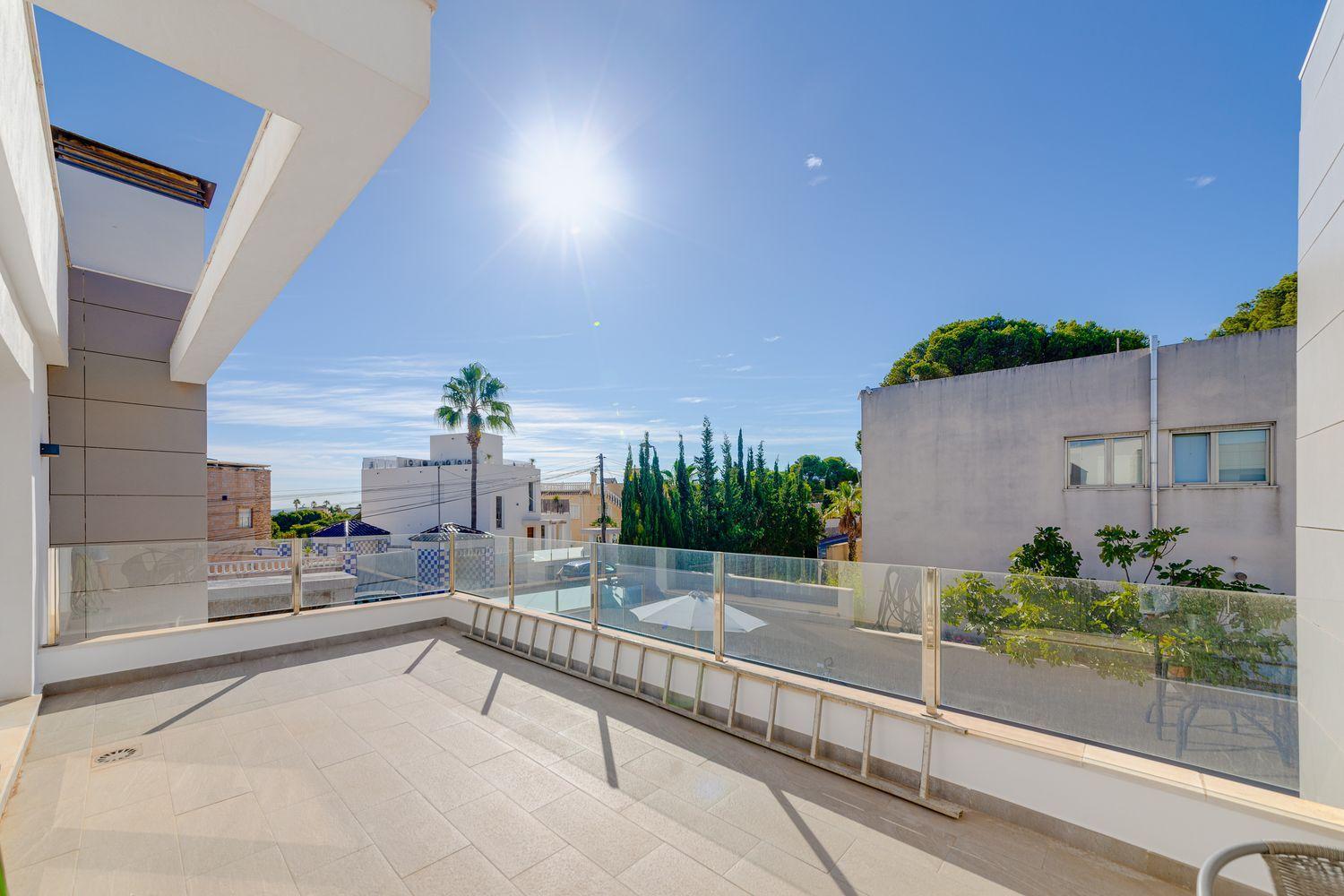 Sunny rooftop terrace with glass railing overlooking a quiet street and modern buildings under a clear blue sky