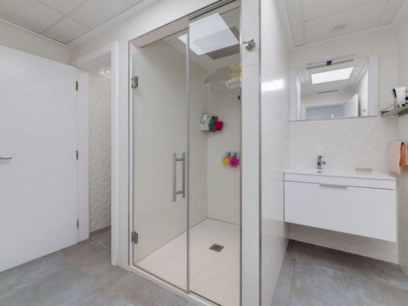 Bright white bathroom with a glass-walled shower and a floating white vanity.