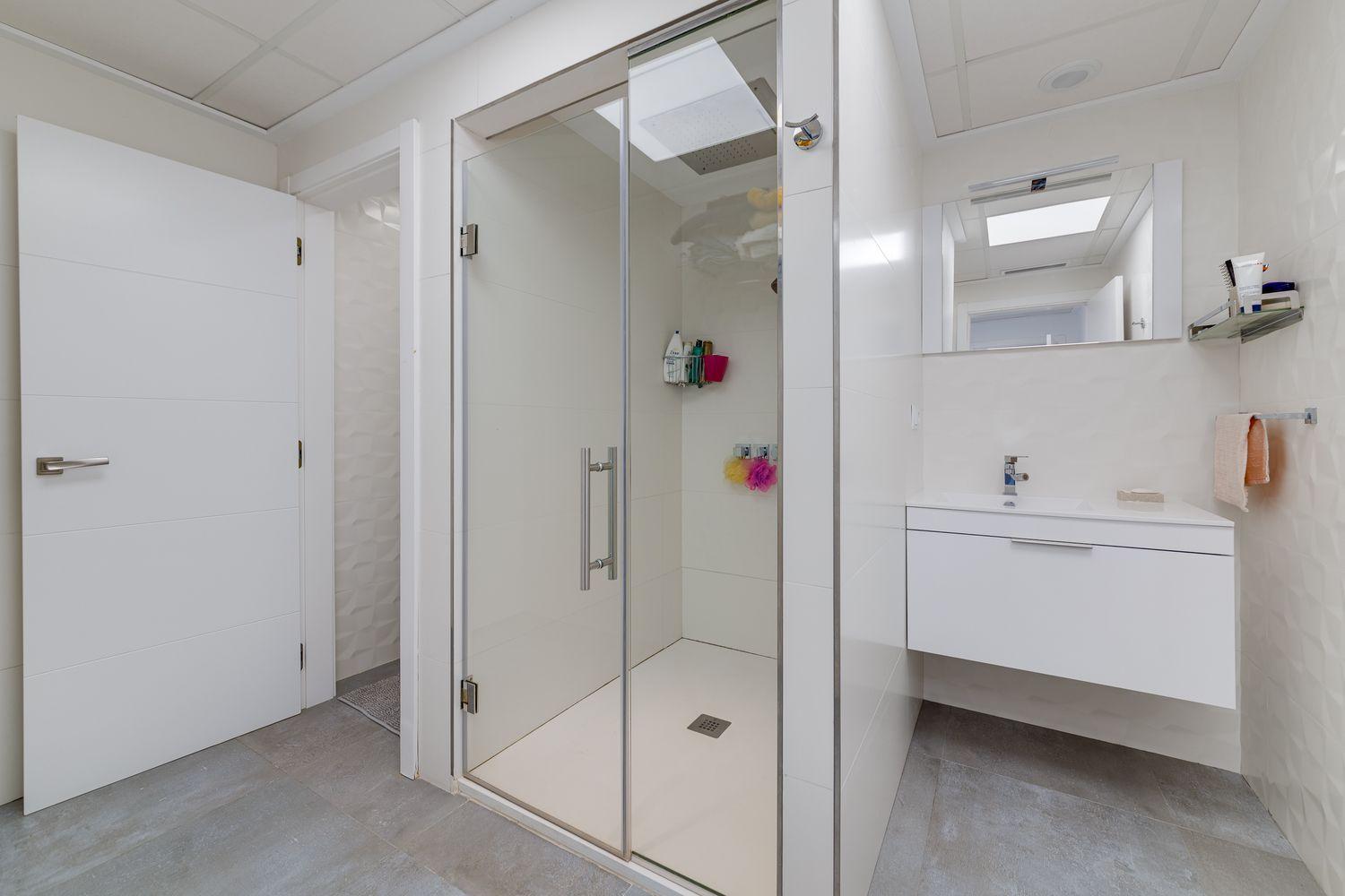 Bright white bathroom with a glass-walled shower and a floating white vanity.