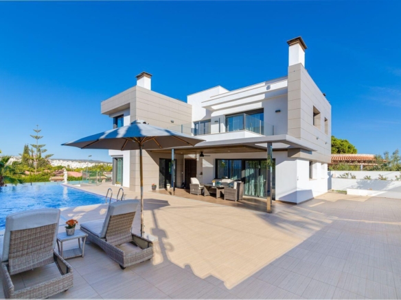 Modern white villa with beige accents, outdoor patio furniture, and a rectangular pool under a blue sky.