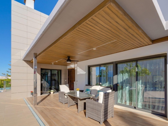Modern outdoor patio with wicker seating around a glass-topped table under a wooden ceiling on a sunny day.