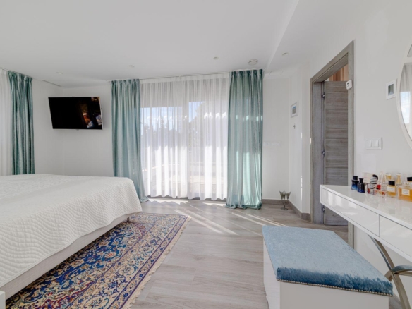 Bright hotel-style bedroom with a white quilted bed, teal drapes, and sheer curtains by large windows