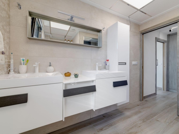 Modern bathroom with white floating vanities, dual sinks, a large horizontal mirror, and a tall white storage cabinet.