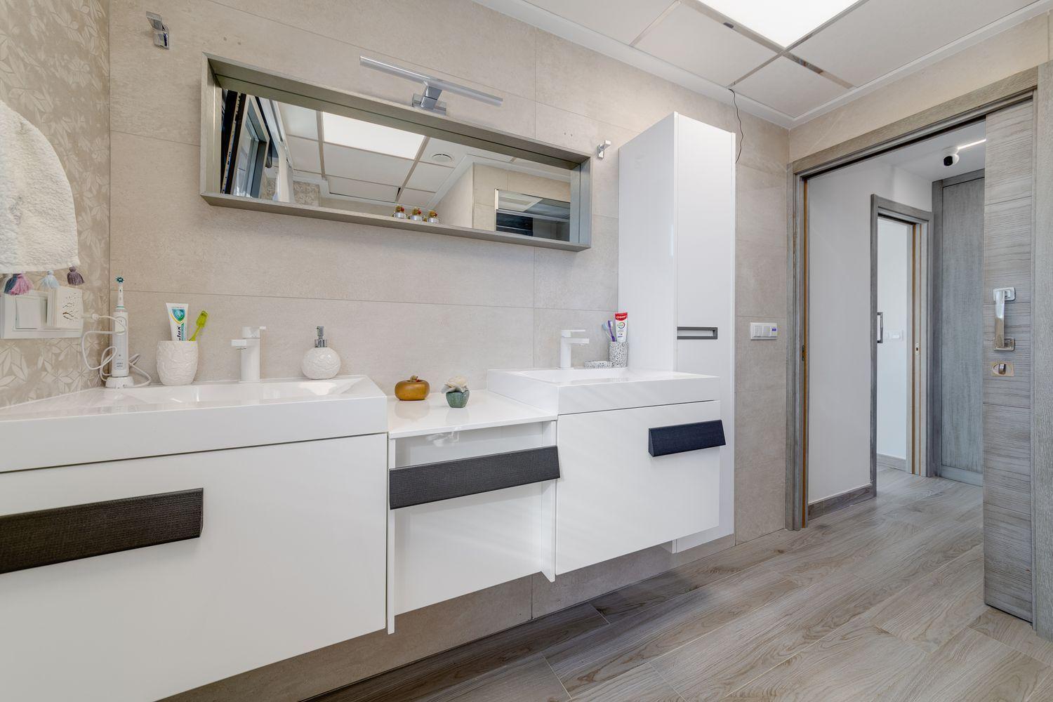 Modern bathroom with white floating vanities, dual sinks, a large horizontal mirror, and a tall white storage cabinet.