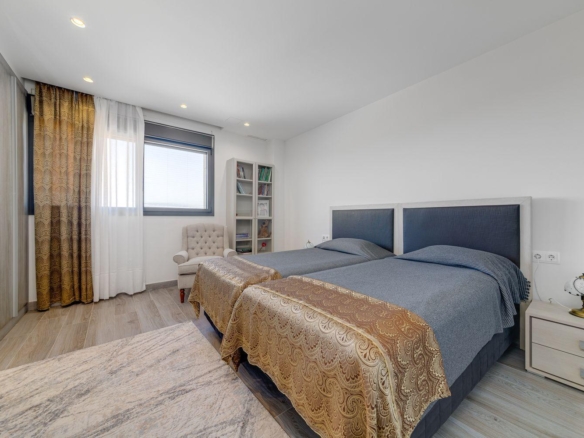 Bedroom with two twin beds side by side, blue upholstered headboards, and gold-patterned bed runners; window with sheer white and gold curtains nearby.