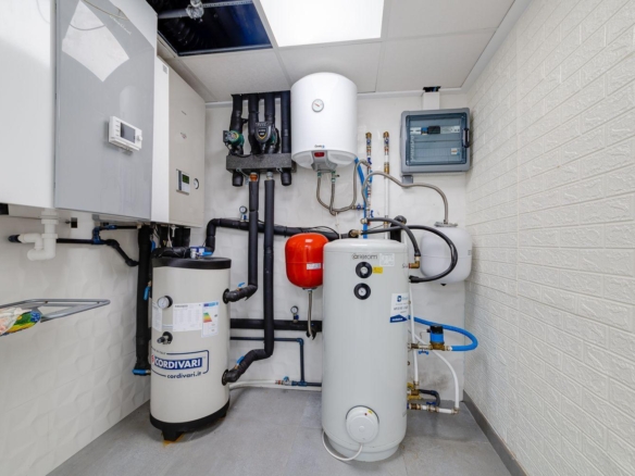 Utility room with multiple water heaters and an expansion tank, exposed pipes and a control panel on the wall