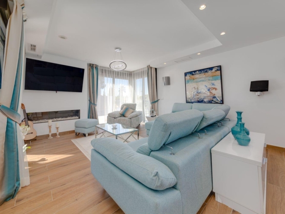 Bright living room with a light-blue sectional sofa, glass coffee table, and a wall-mounted TV above a linear fireplace.