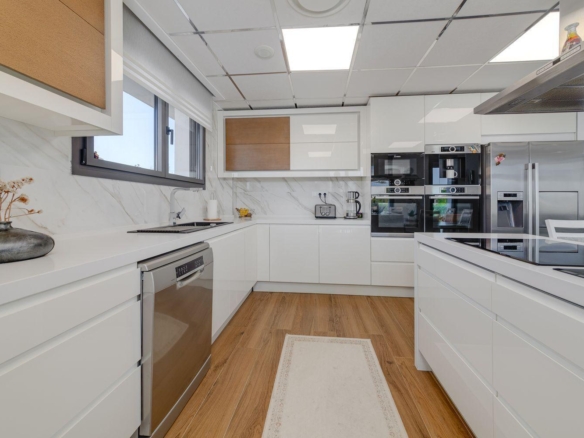 Bright modern U-shaped kitchen with white cabinets, wooden floor, stainless steel appliances, and a central island.