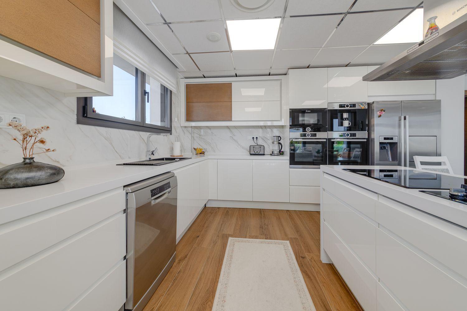 Bright modern U-shaped kitchen with white cabinets, wooden floor, stainless steel appliances, and a central island.