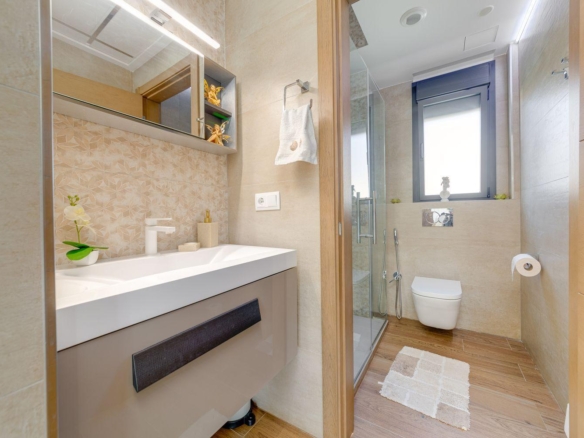 Modern bathroom with beige tiles, white sink vanity, wall mirror, glass shower, and wall-mounted toilet.
